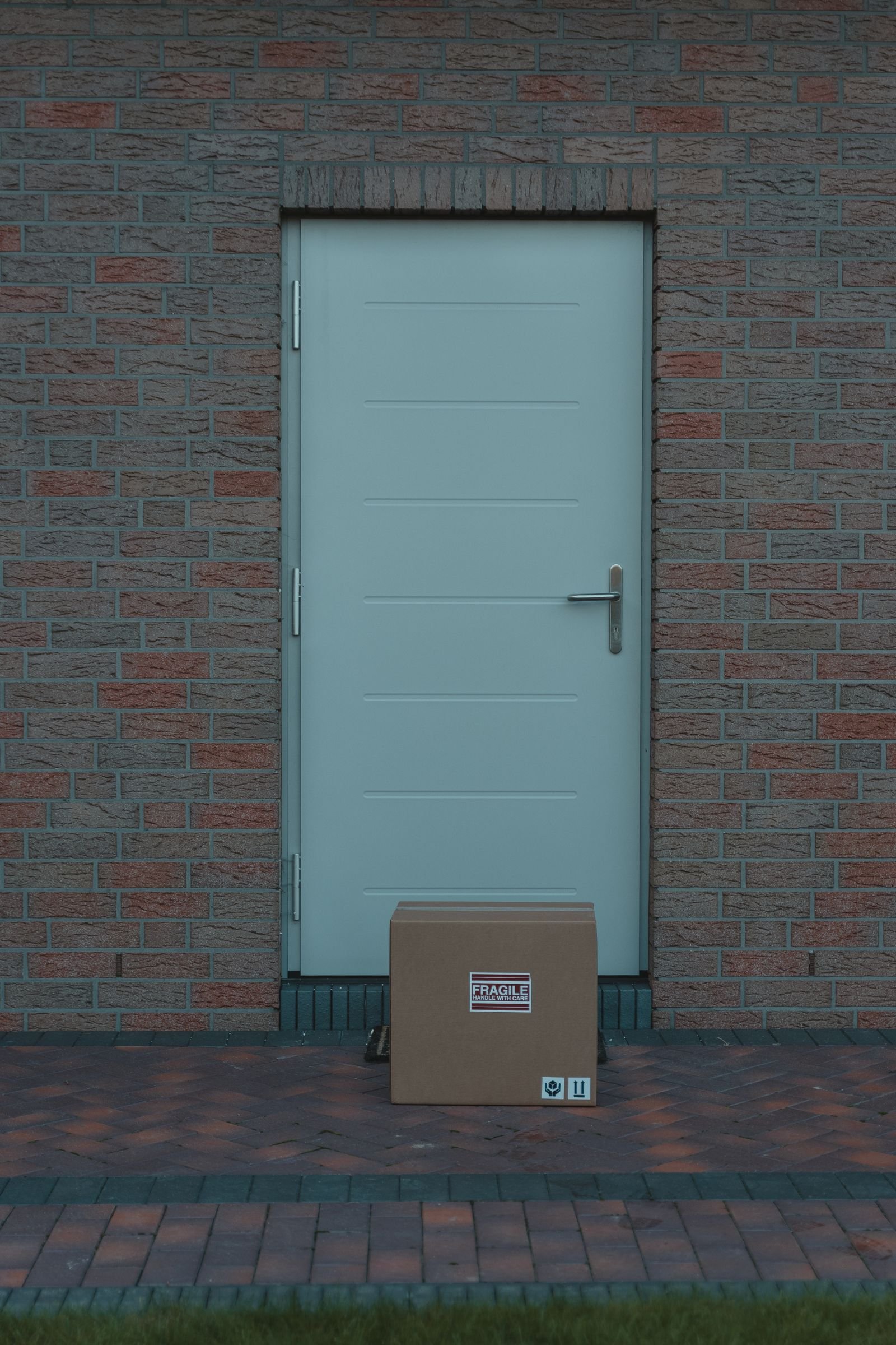 A plain brown cardboard box with a fragile label, left on the doorstep of a pale front door in a brick house. A plain brown cardboard box with a fragile label, left on the doorstep of a pale front door in a brick house.
