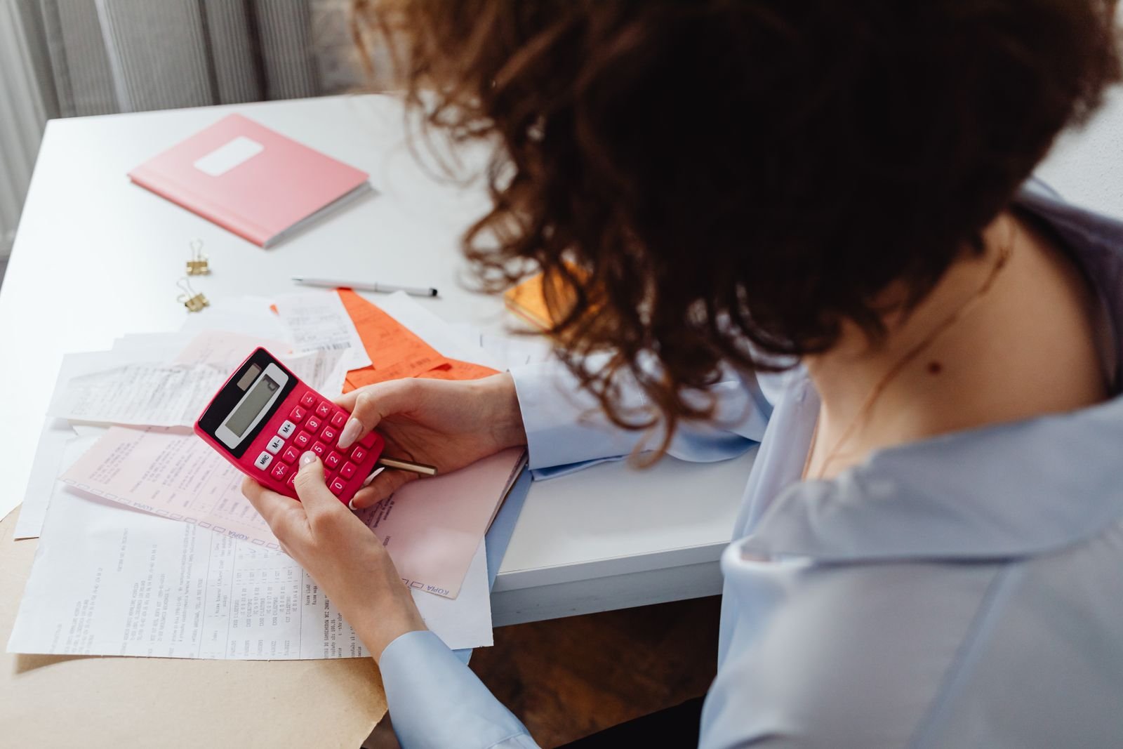 A person at a desk using a small calculator while working through a spread of receipts and paperwork. A person at a desk using a small calculator while working through a spread of receipts and paperwork.